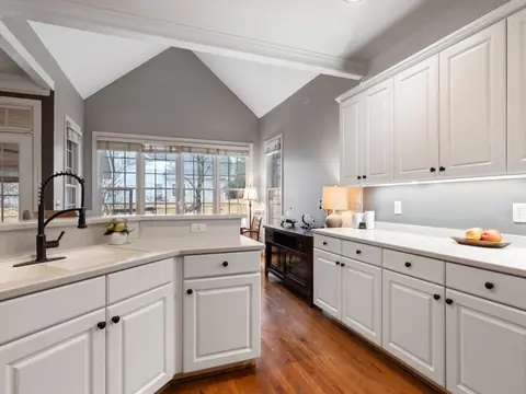 A clean modern kitchen with white cabinets, clear wiped counters and large windows